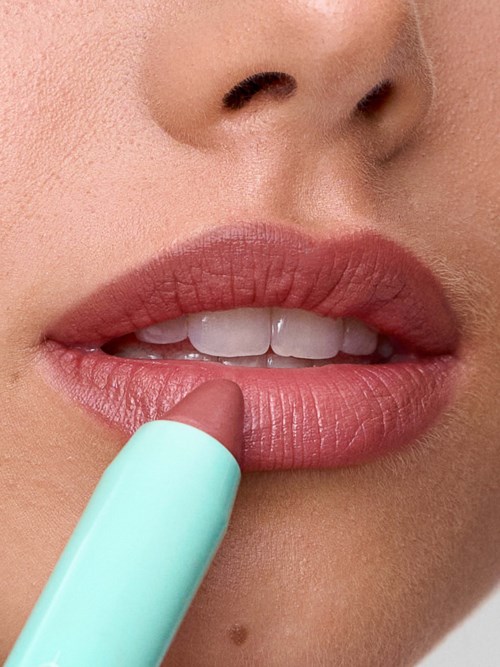 Close-up of lips and part of face, with a stick applying lipstick. Focus on lips and small beauty details.