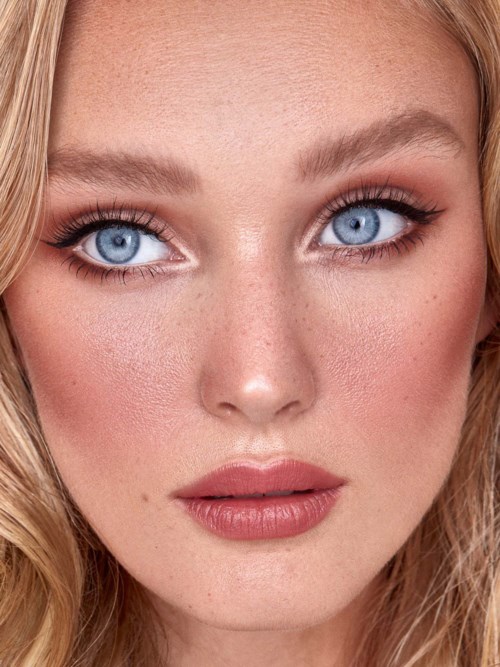 A woman with blonde hair and blue eyes looks directly at the camera, with makeup and smooth skin.