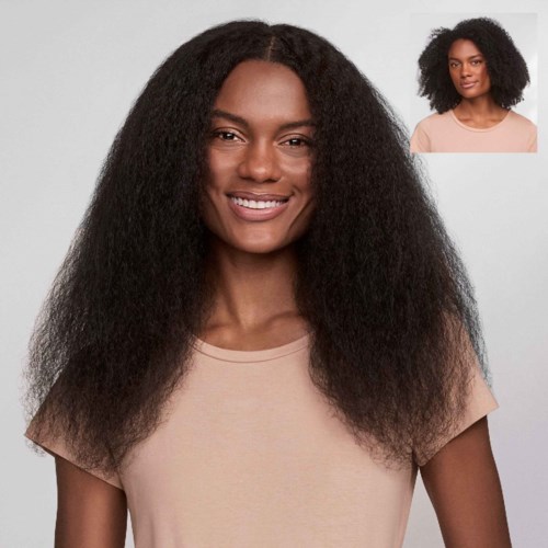 A woman with long, voluminous curly hair, smiling, wearing a beige t-shirt.