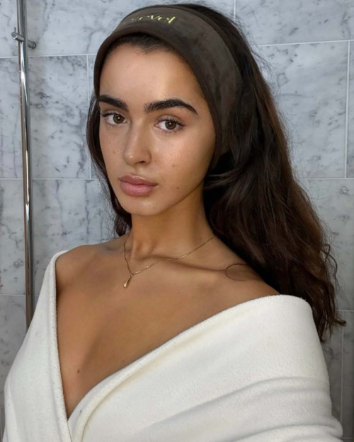 Eine junge Frau mit langen dunklen Haaren, trägt ein schwarzes Stirnband und ein weißes Schulterkleid.
