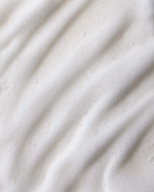 Glatte weiße Oberfläche mit weichen Schatten, möglicherweise Stoff oder Papier, mit sanften Falten und kleinen Punkten.