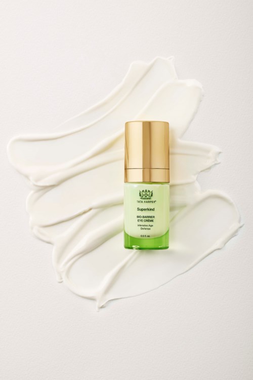 A small green and gold bottle of eye cream on white cream spread. The bottle has a label and a gold cap.