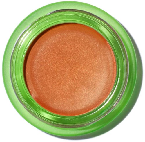 A green container with a peach-colored cream or makeup product inside. The container has a clear lid.