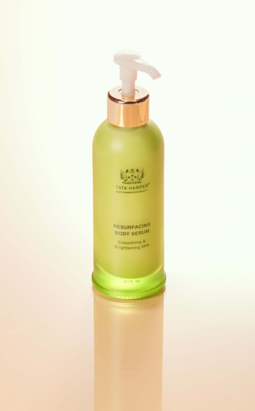 En grön flaska med en vit pump, märkt som Tata Harper resurfacing body serum, står på en ljus yta.