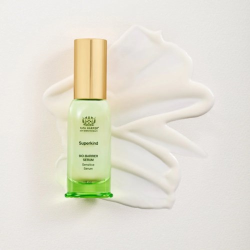 Green serum bottle with a gold cap, surrounded by white cream on a white background.