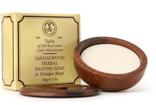 A wooden bowl with white shaving soap and a matching wooden lid, and a yellow box with black text.