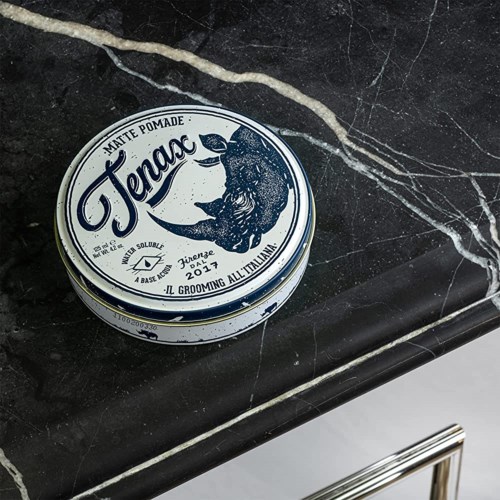 A round tin of Tenax matte pomade on a black marble surface with white veins.
