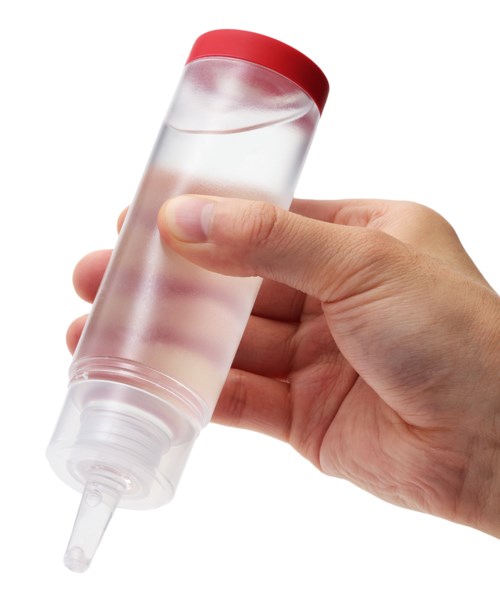 A hand holds a transparent bottle with a red cap, containing clear liquid, and a nozzle for squeezing out contents.