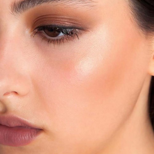 Close-up van een vrouwelijk gezicht met make-up, vooral rond het oog en de lippen, met een gladde huid en zachte kleuren.