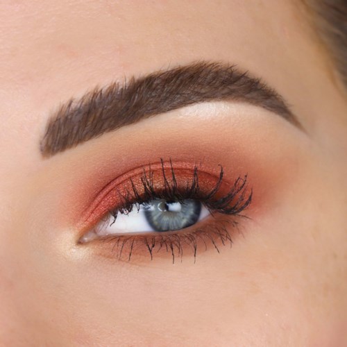 Close-up van het oog van een vrouw met make-up, inclusief oogschaduw, eyeliner, mascara en een goed gevormde wenkbrauw.