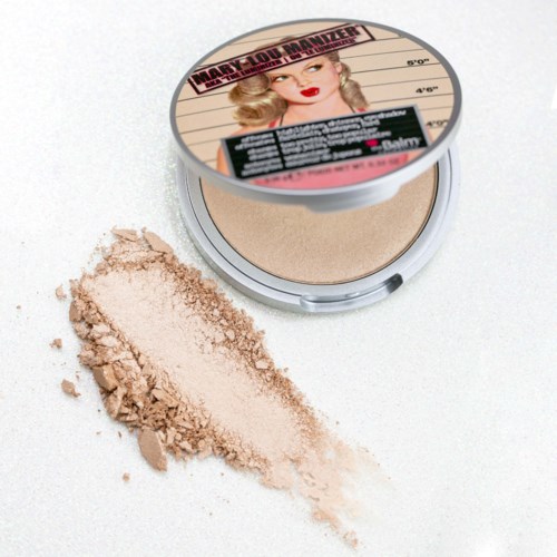 Ett kompakt puder med en kvinnas illustration på etiketten, lite puder spillt bredvid, på en vit bakgrund.