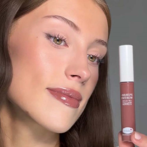 Een vrouw met glanzende lippen en bruin haar die een lipgloss vasthoudt.