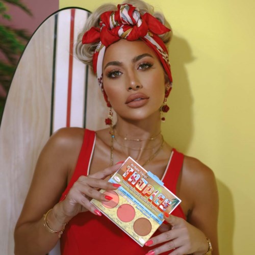 Een vrouw met gestyled blond haar, rood topje en rood hoofddoekje houdt een make-up palette met kleuren.
