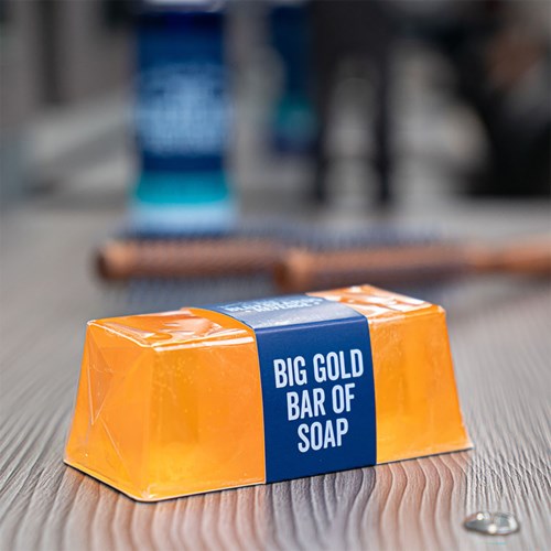 A bar of soap wrapped in orange packaging with a blue label that says 'Big Gold Bar of Soap' on a wooden surface.