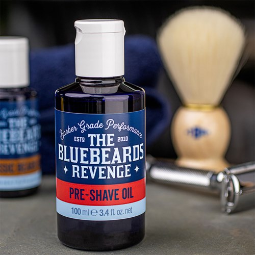 A bottle of pre-shave oil with a blue and red label and related shaving tools in the background.