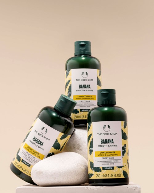 Tre grønne flasker med Banana sjampo, balsam og dusjsåpe fra The Body Shop vist med hvite steiner.