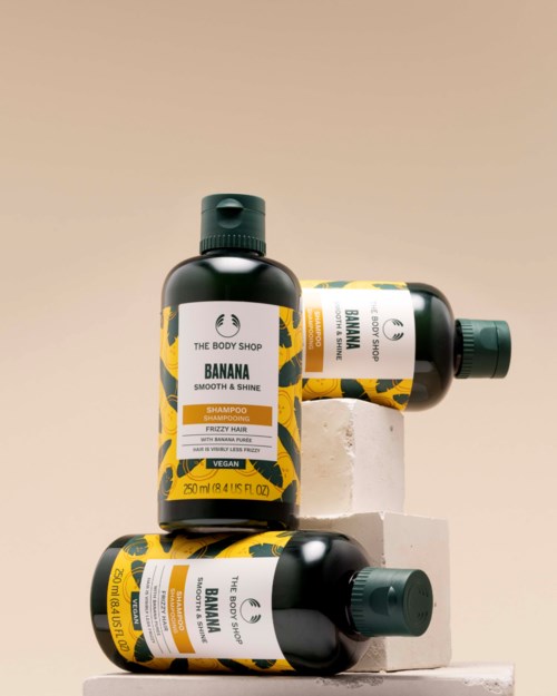 Tre flasker med bananshampoo og balsam fra The Body Shop vises på hvite blokker.