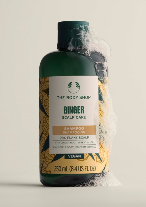 Eine grüne Flasche von The Body Shop Ginger Scalp Care Shampoo mit Schaum, als vegan gekennzeichnet, für trockene, schuppige Kopfhaut.