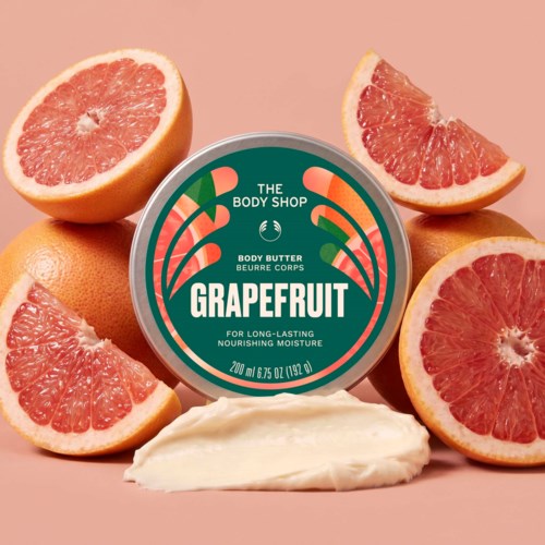 Grapefruit scented body butter jar surrounded by fresh grapefruit halves on a peach-colored background.