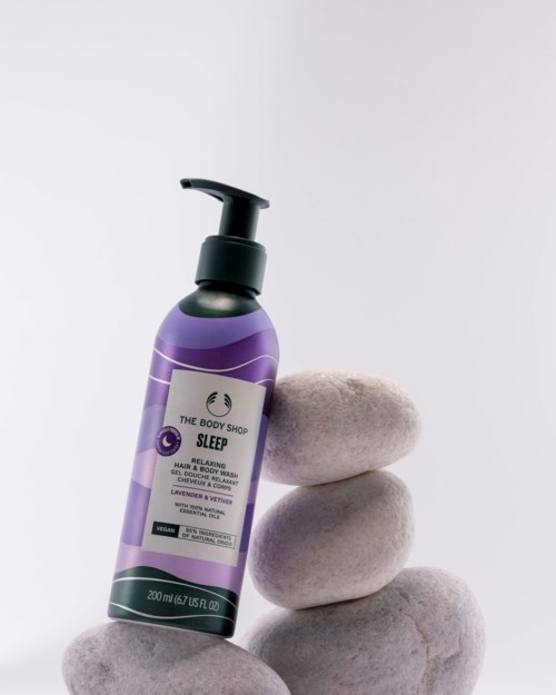 Lavendel- og vetiver-søvnkrem i en lilla flaske med pumpe, hvilende på tre lyse grå steiner.