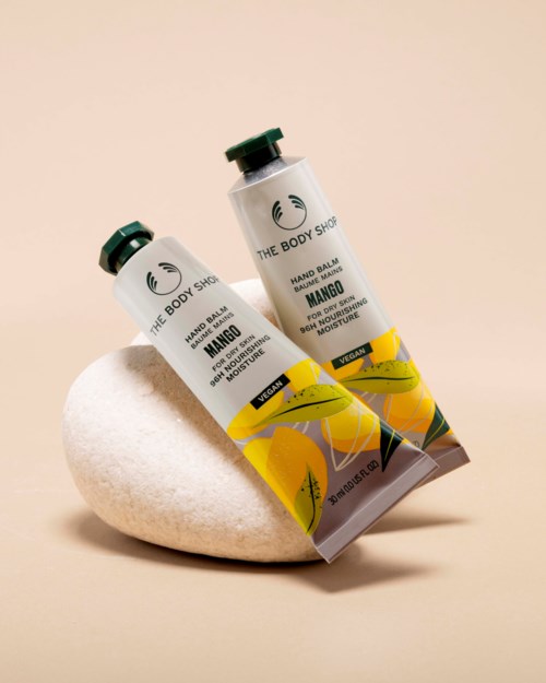 To rør med mangosmakende håndbalsam fra The Body Shop hviler på en glatt hvit steinflate.