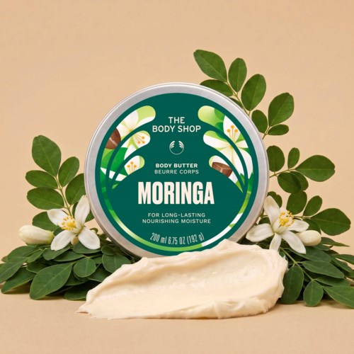 Moringa kroppssmörjkruka med kräm som bretts ut och gröna blad samt vita blommor runt den.