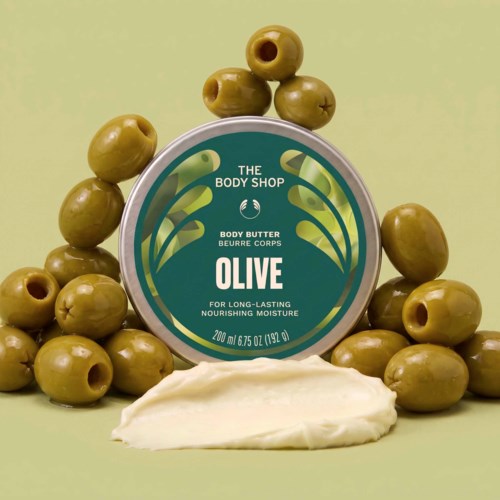 Oliv kroppssmörj behållare omgiven av gröna oliver och lite Creme längst ner.