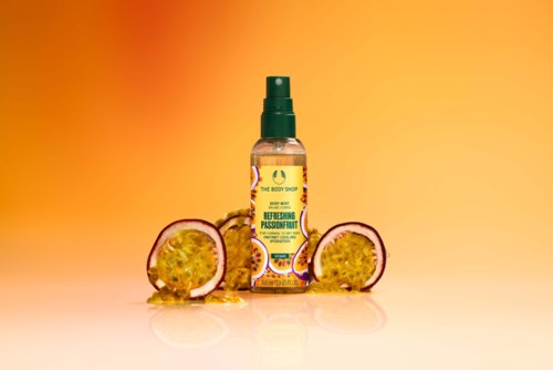 Eine Sprühflasche mit Passionfrucht-Erfrischung auf einem Farbverlauf-Orangenhintergrund, umgeben von Passionfruchtstücken.