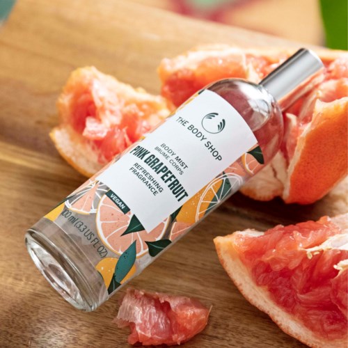 Eine Körpersprühflasche mit Grapefruit-Duft neben Grapefruit-Stücken auf Holz.