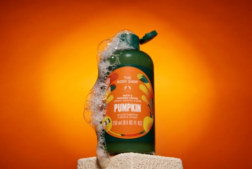 Pumpkin scented shower cream bottle from The Body Shop with soap bubbles and an orange background.