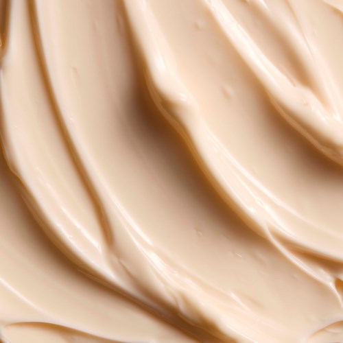 Glatt, kremaktig beige prøve av sminke eller hudpleieprodukt. Svingete tekstur med myke høylys.