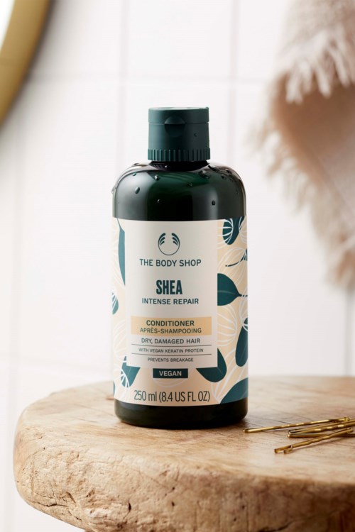 Eine dunkelgrüne Flasche Shea Intensive Repair Conditioner auf einer Holzoberfläche, mit einer Klammer in der Nähe.