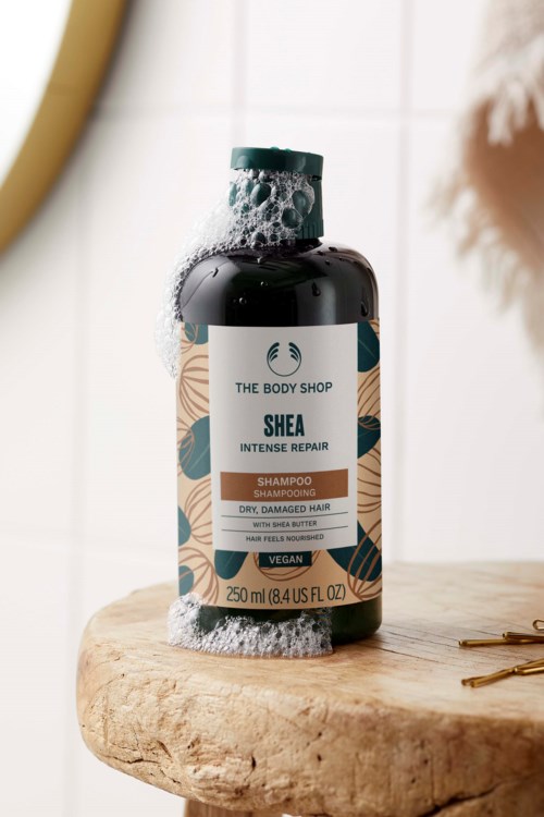 Eine Flasche Shea Intensive Repair Shampoo von The Body Shop mit Schaum auf der Oberseite, auf einer Holzoberfläche.
