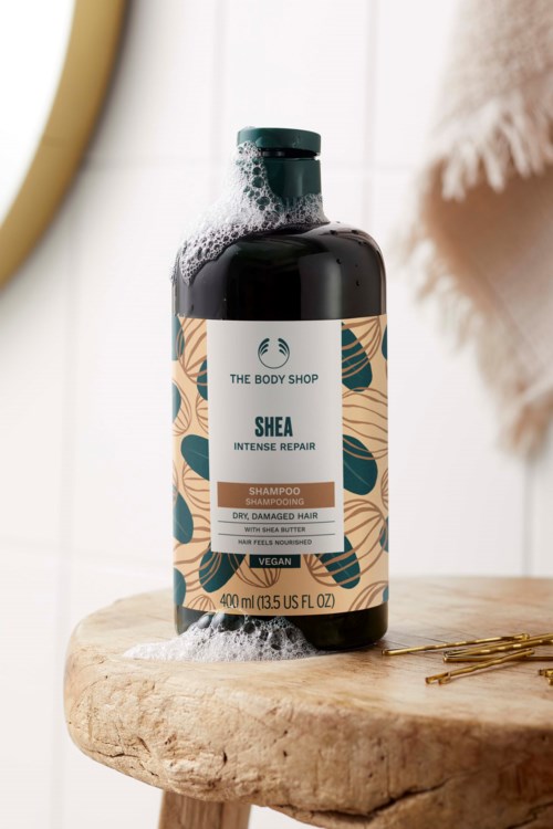 Eine Shampooflasche mit Blumenmuster, steht auf einer Holzoberfläche, mit etwas Schaum oben.