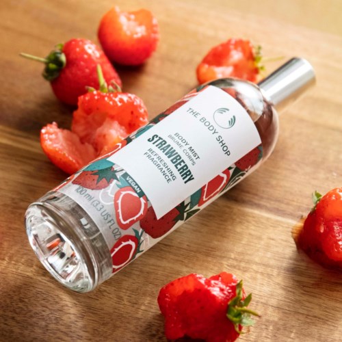 Eine Flasche mit der Aufschrift 'Strawberry' Körperspray, umgeben von frischen Erdbeeren auf einer Holzoberfläche.