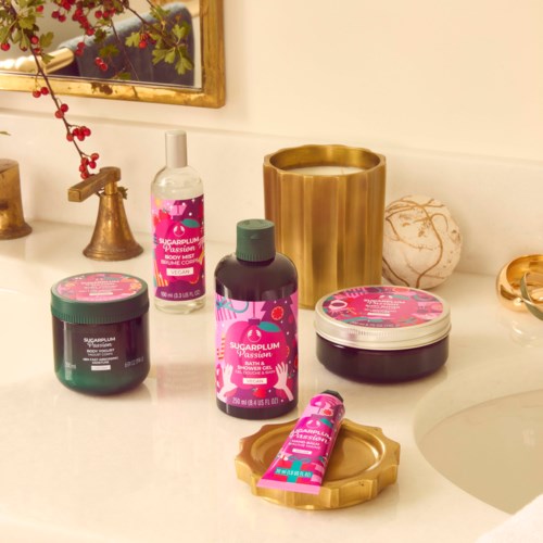 Various bath products with pink labels, a gold vase, and decorative items on a white counter.