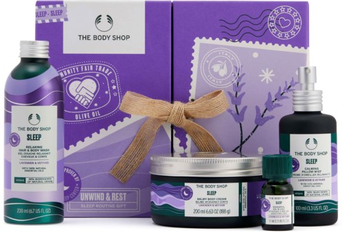 Ett lila presentset med sömnprodukter, inklusive lotion, spray, kräm och oljor, med en låda knuten med ett beige band.