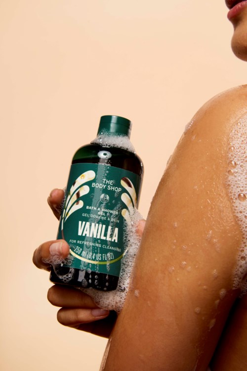 Person holds a bottle of vanilla body wash while taking a shower.