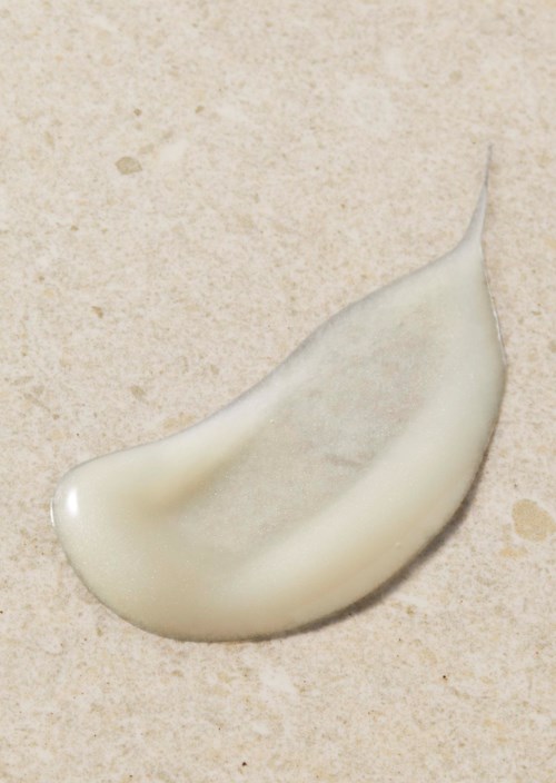 A drop of white lotion or cream on a beige surface.