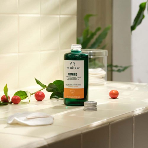 A bottle of Vitamin C toner on a tiled surface with scattered red berries and a gray cap.