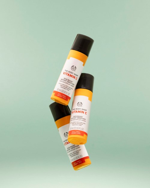 Tre flaskor av Vitamin C-bodylotion med svarta lock och orange- och vita etiketter, placerade på ljusgrön bakgrund.