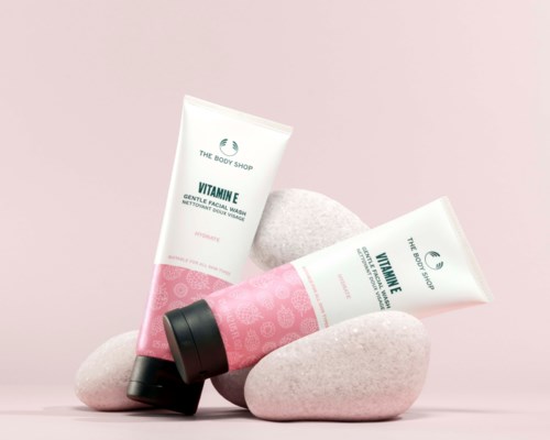 Två tuber av The Body Shop Vitamin E gentle facial wash med svarta lock, placerade på rosa stenar mot en rosa bakgrund.