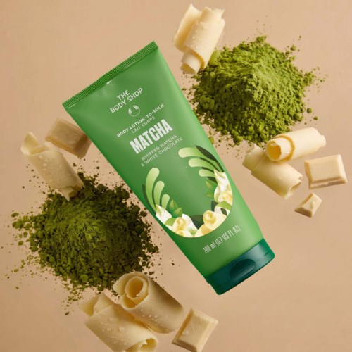 The Body Shopin vihreä body lotion -tölkki, jonka ympärillä on matchajauhetta, valkoisia suklaalevyjä ja matchanvärisiä esineitä.