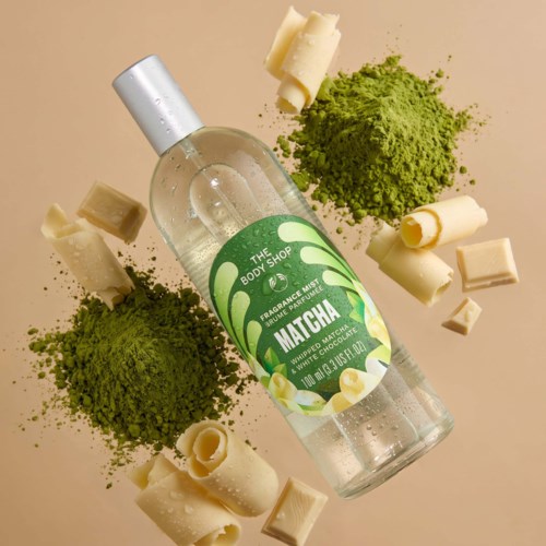 Läpinäkyvä pullo nimeltä Matcha, ympäröi vihreä matchajauhe ja valkoiset suklaapalikat.