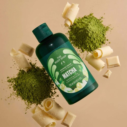 Vihreä The Body Shop Matcha -suihkuvoidepullo, ympärillä matcha-jauhetta ja valkoisia suklaata.