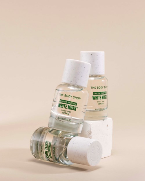 Tre små parfymeflasker merket White Musk fra The Body Shop, med grønn og hvit innpakning, stablet og lente mot hvite blokker.
