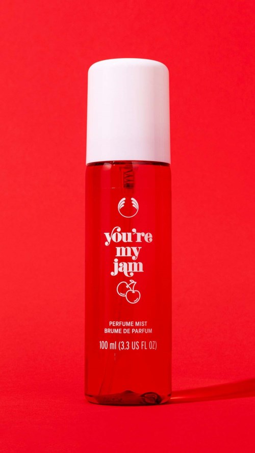 Rotes Parfümspray mit weißem Deckel und verspieltem Text, Liebesthema mit Kirschenbild, auf rotem Hintergrund.