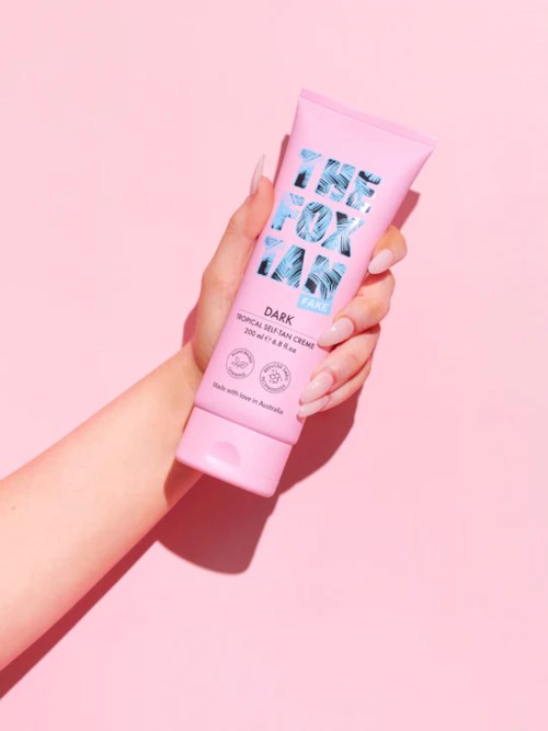A hand holding a pink tube of skincare cream against a pink background.