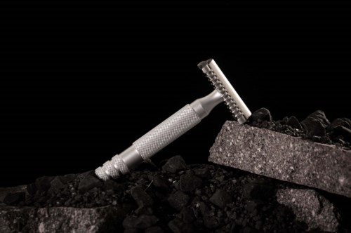 A safety razor leaning on a bed of black coal, with a small container of more coal nearby.