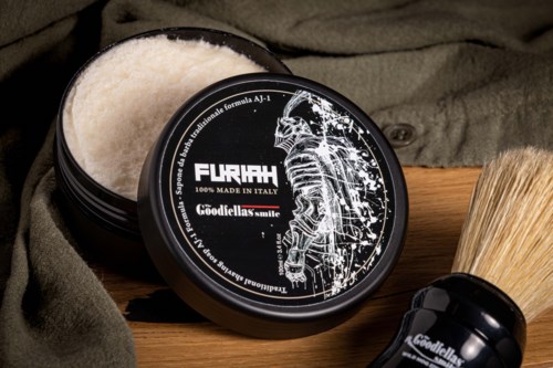 A black container of shaving cream with a skeleton design, a shaving brush, and a towel on a wooden surface.
